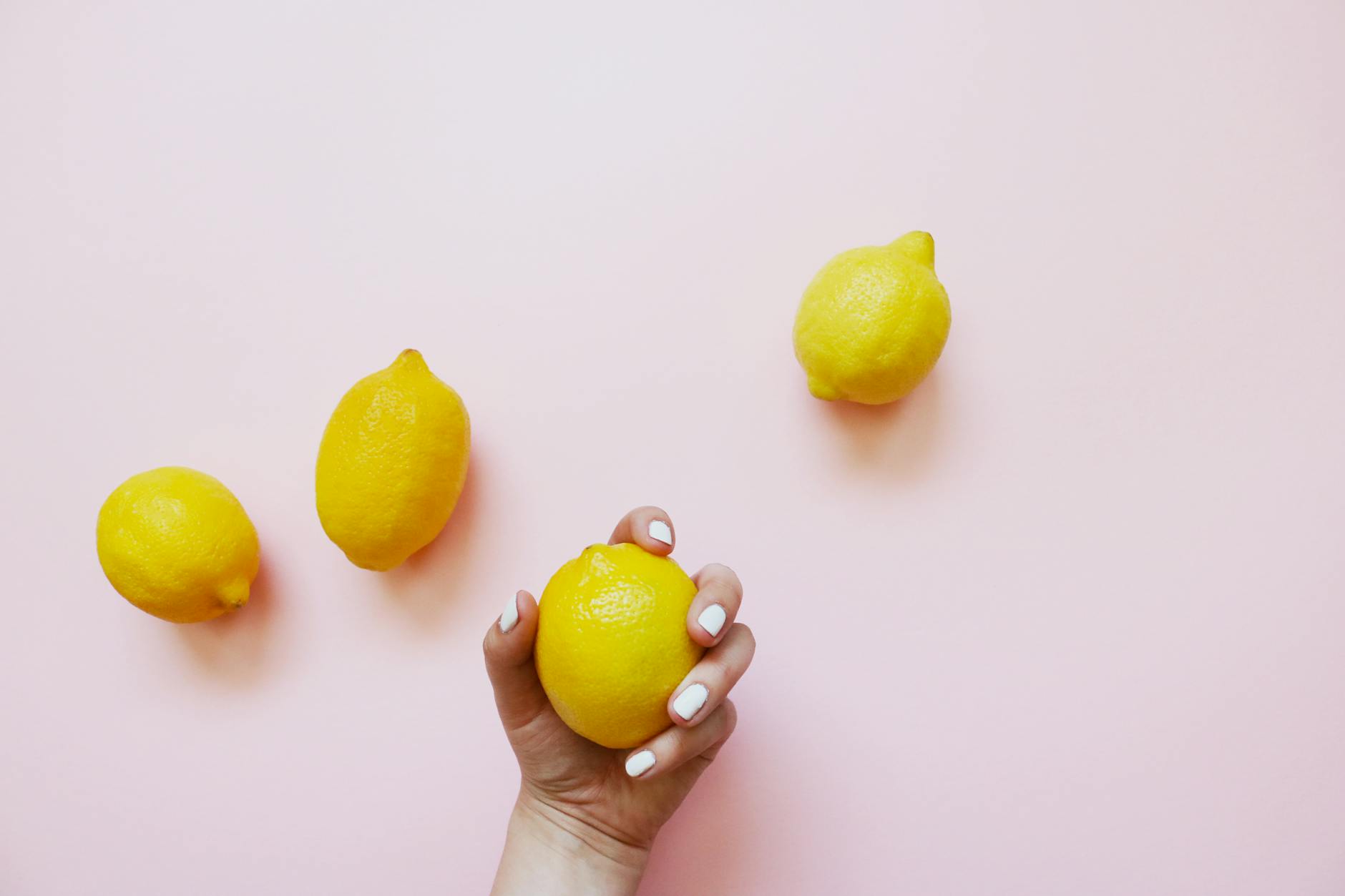 A hand holding a fresh lemon on a soft pink background, symbolizing the gentle approach to rebuilding clitoral sensation.