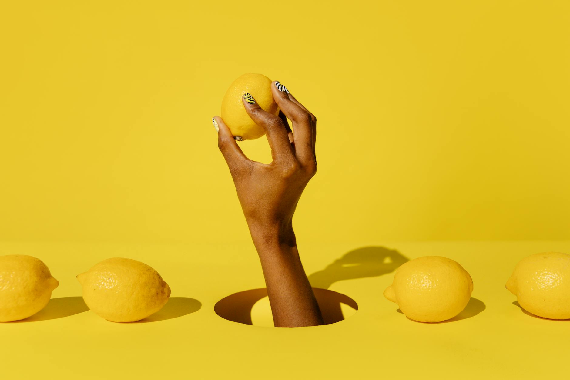 A hand holding a fresh lemon against a vibrant yellow background