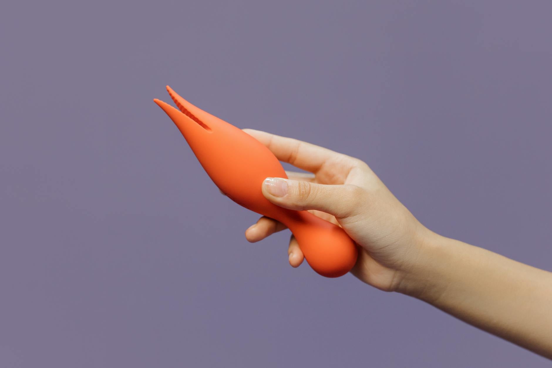 Close-up of a hand holding a lemon-colored vibrator against a minimalist purple backdrop, showcasing modern sensuality